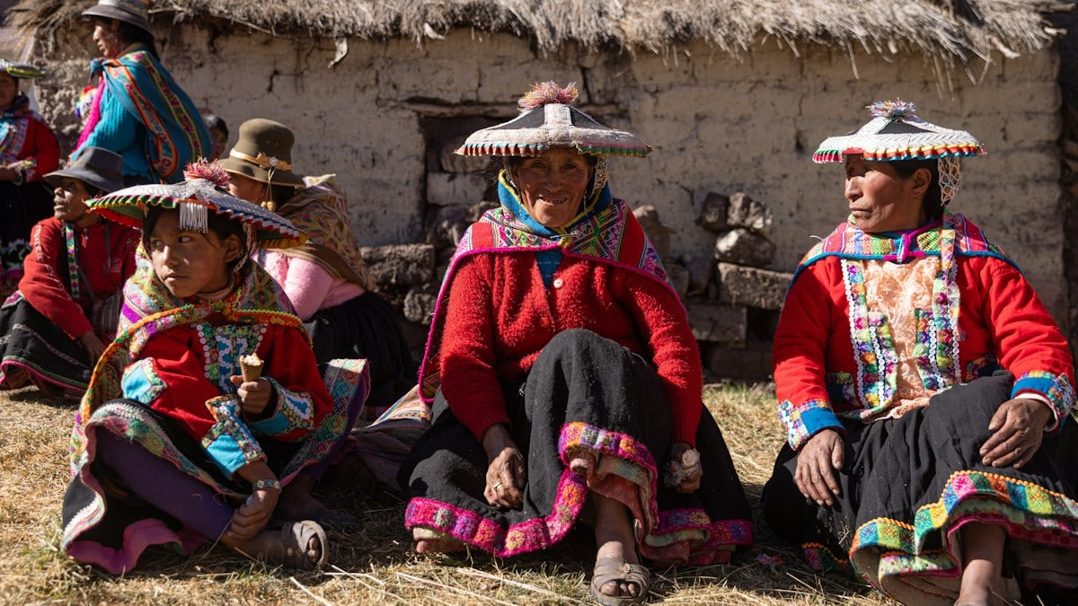A group of people sitting next to each other in front of a hut